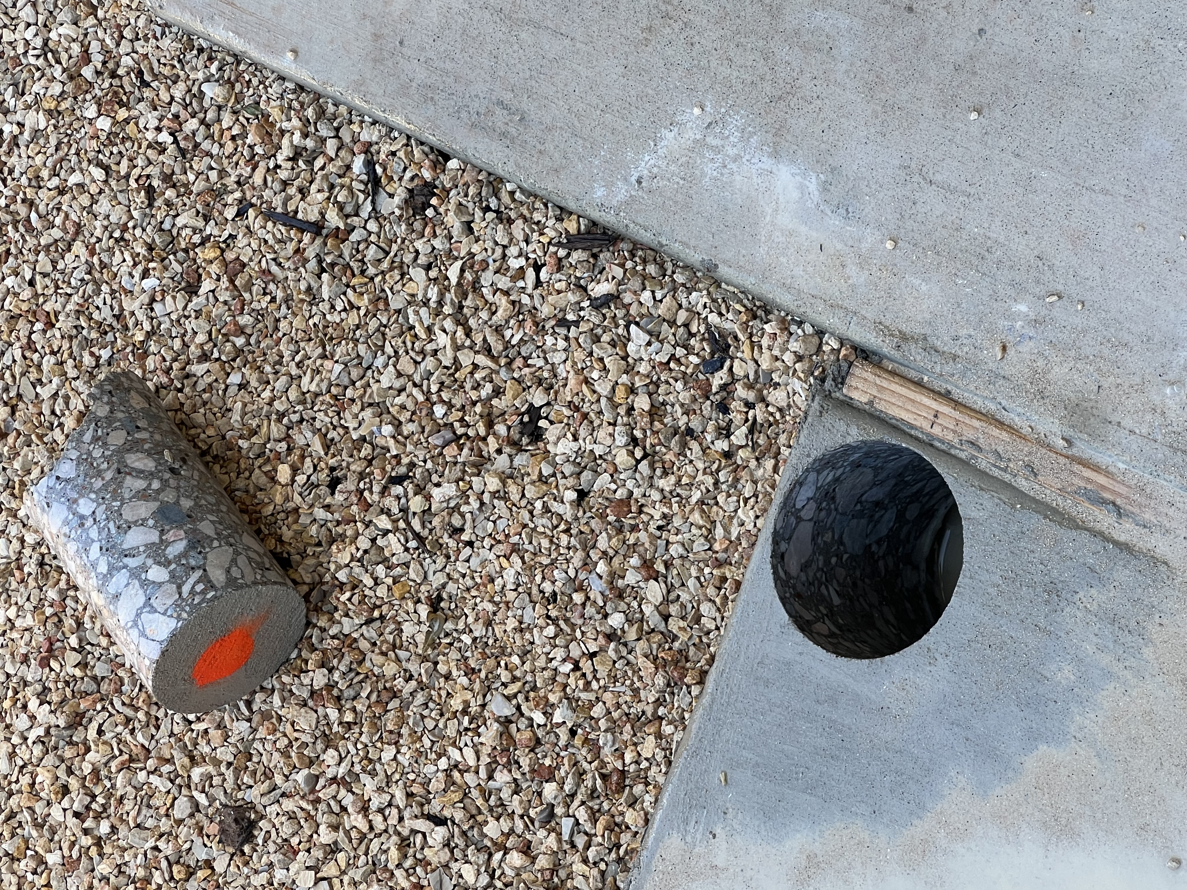 Extracted concrete core sample next to a freshly drilled hole in a slab